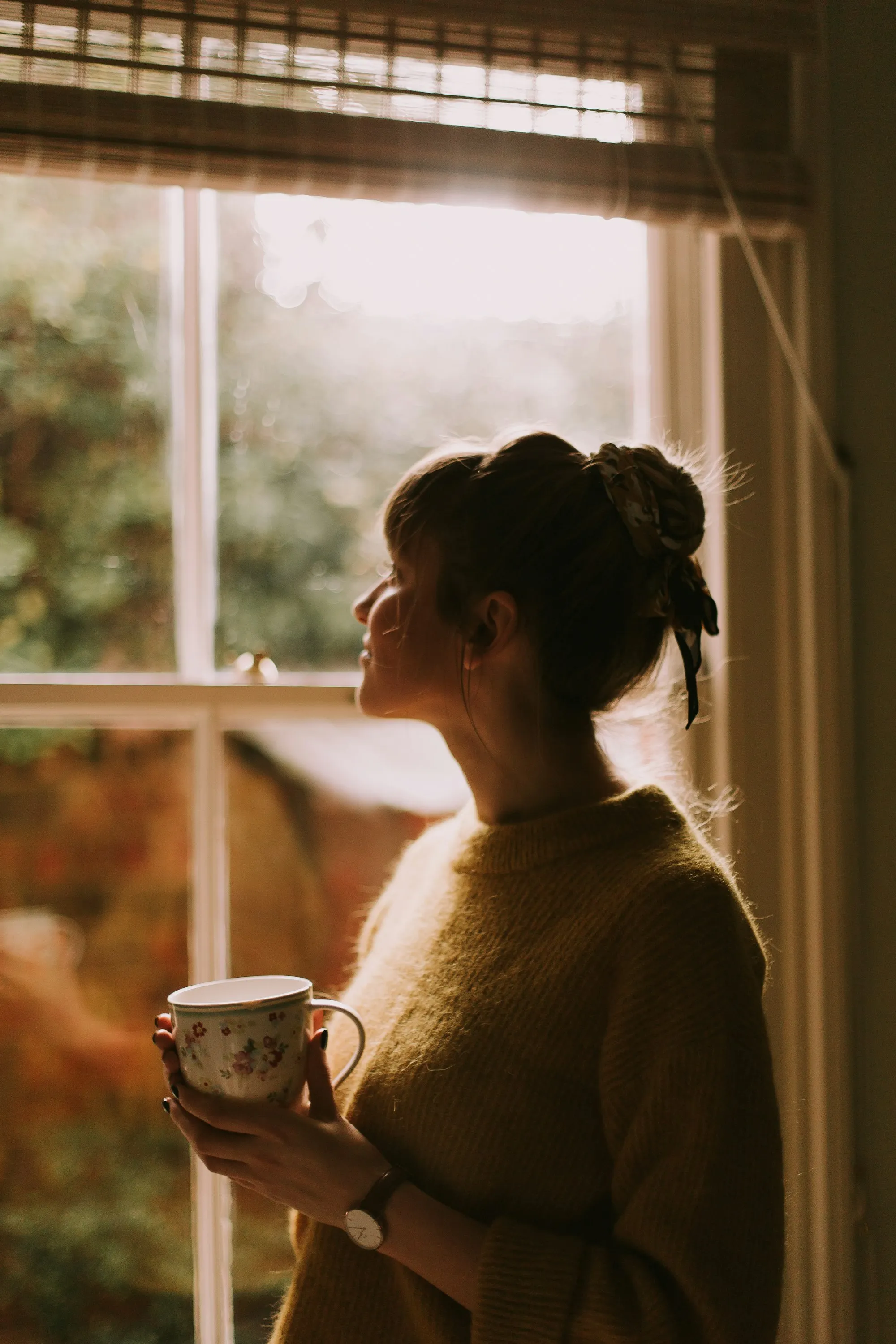 Woman holding a mug by a bright window at home