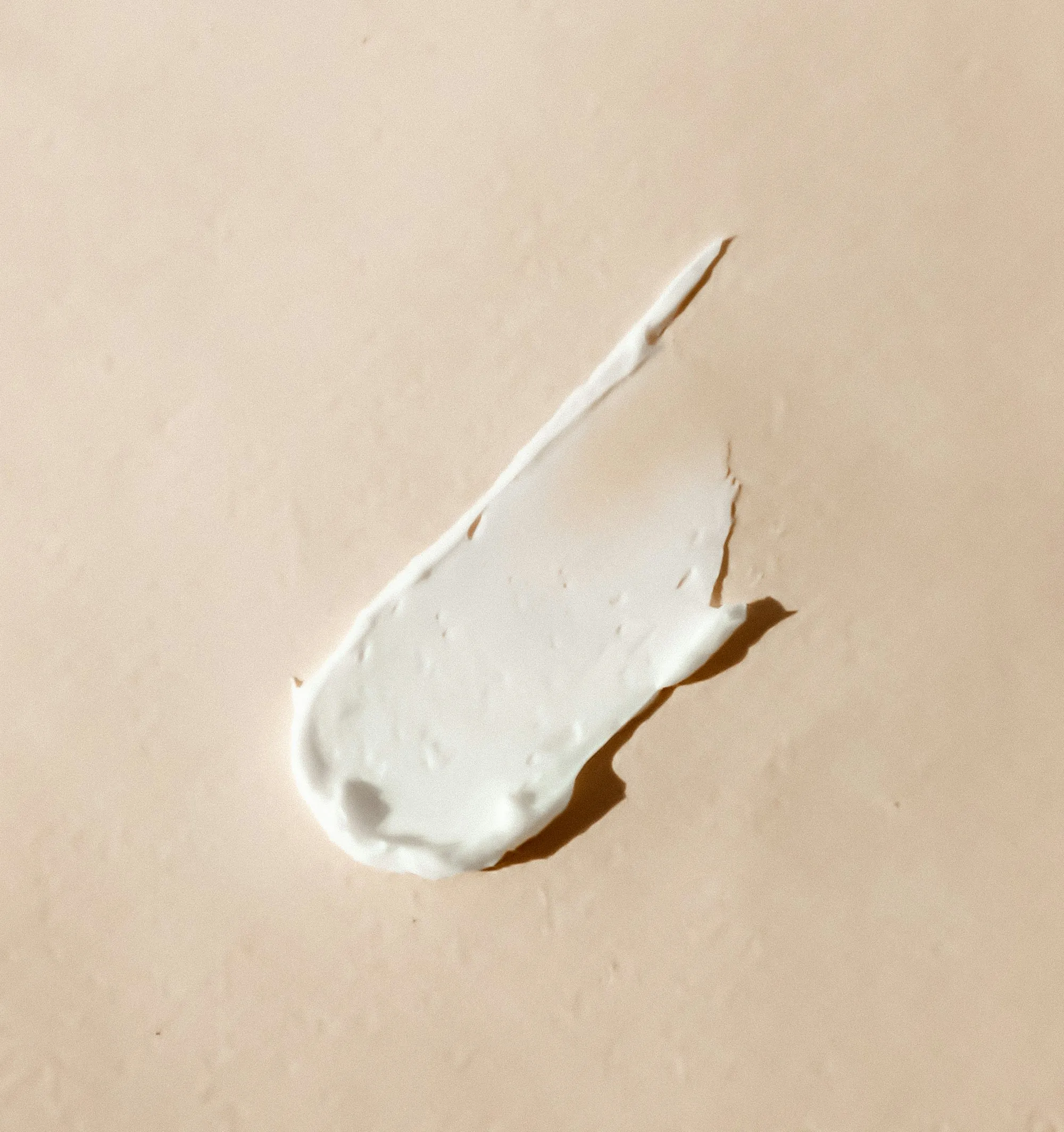Swipe of white moisturizer on a sand-colored background