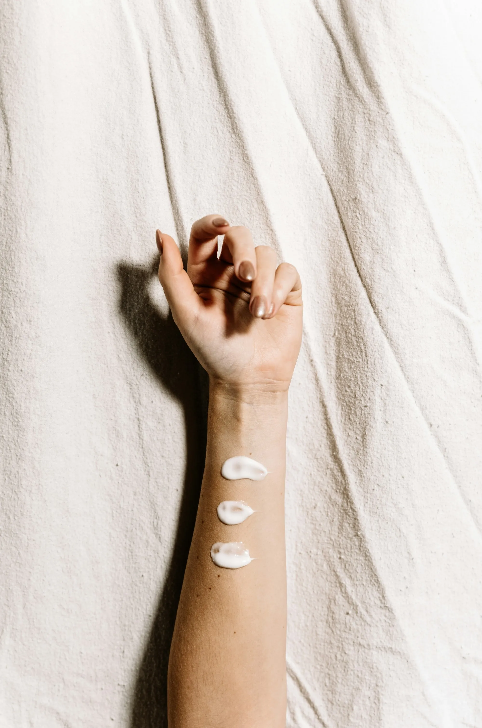 Dots of lotion on a forearm resting on white linen