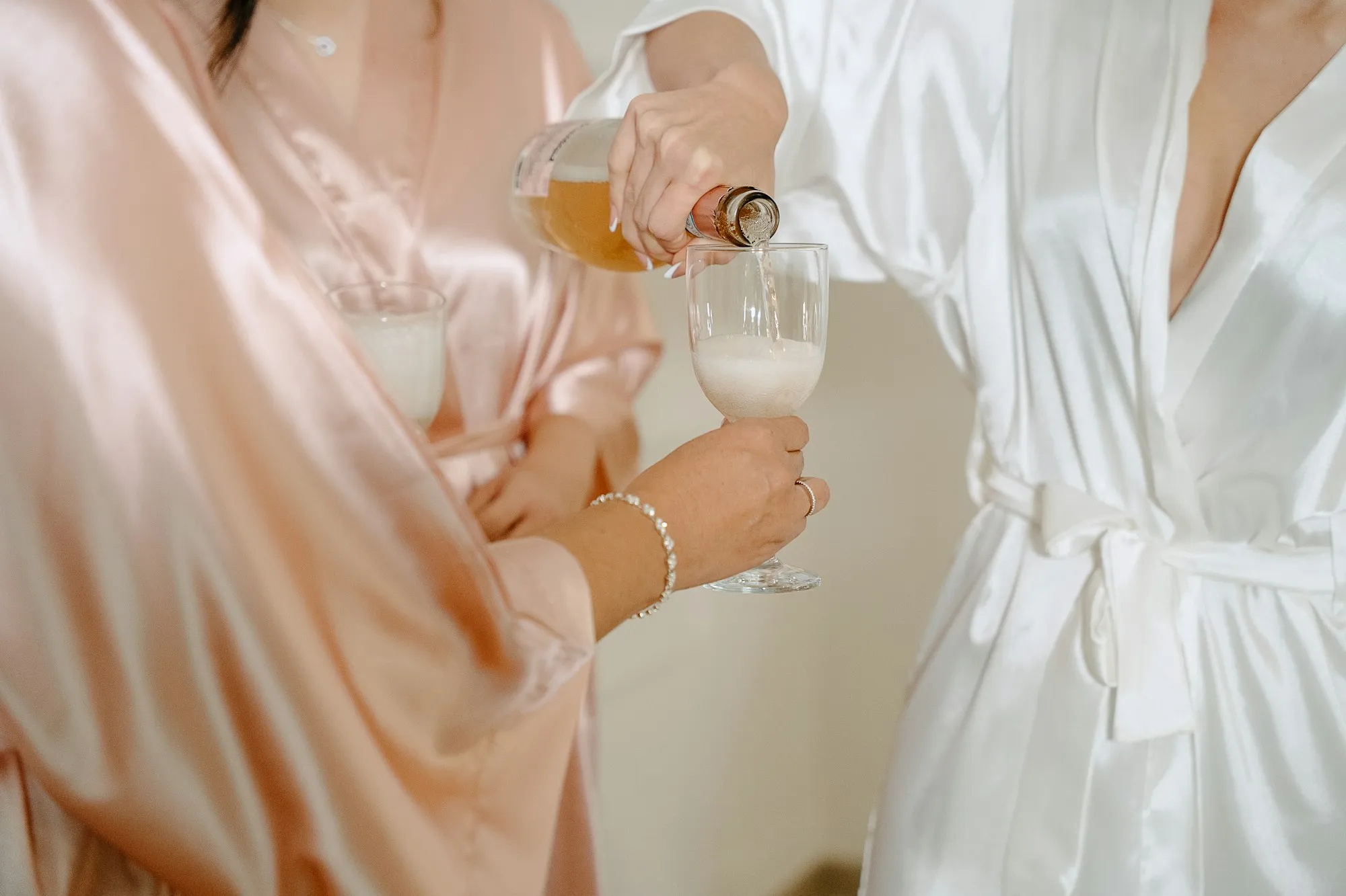 Friends in satin robes pouring sparkling wine while getting ready