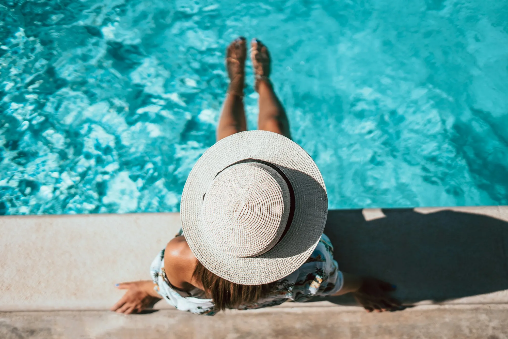 Person in a wide sun hat sitting at the edge of a turquoise pool