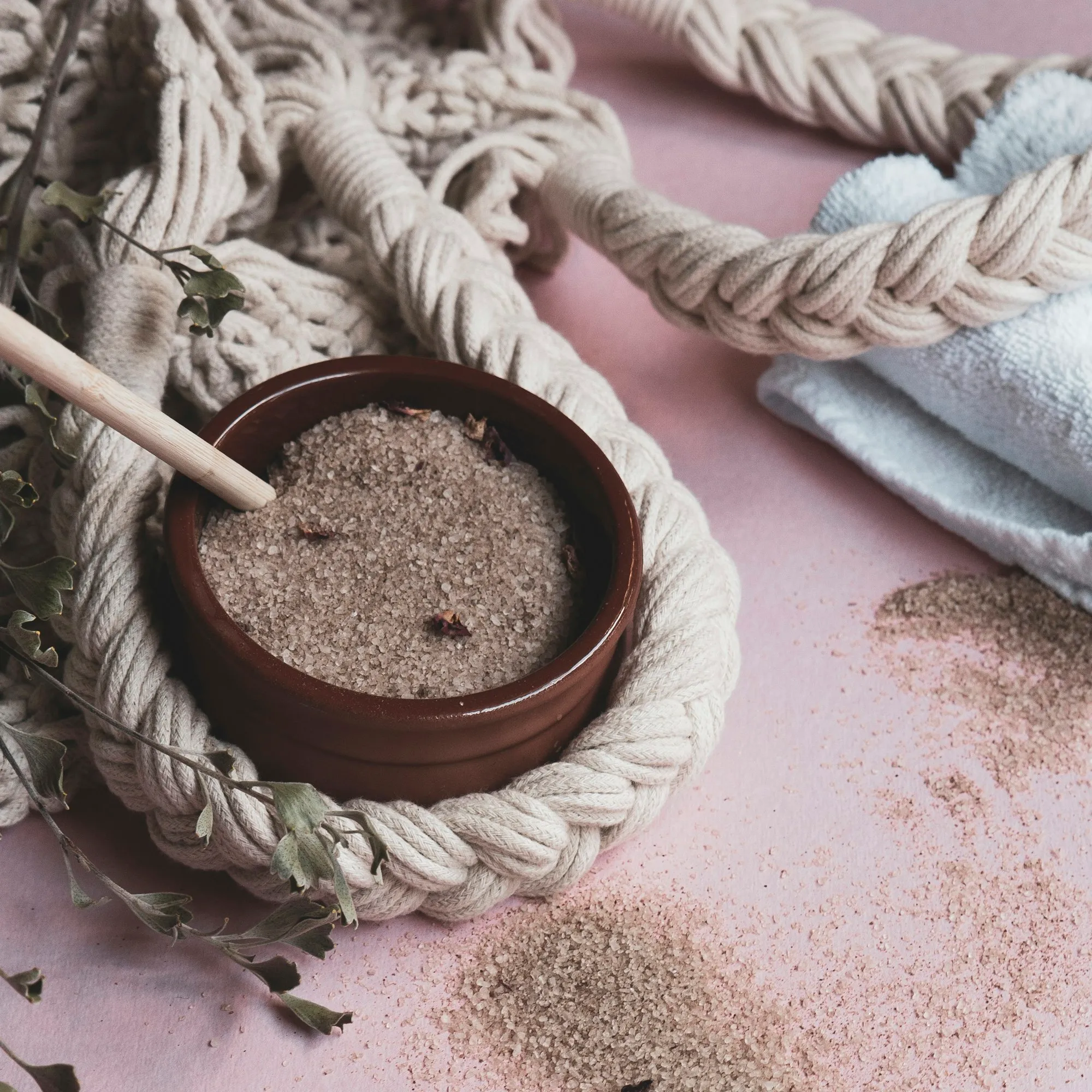 Bowl of body scrub with a wooden spoon on a pink surface